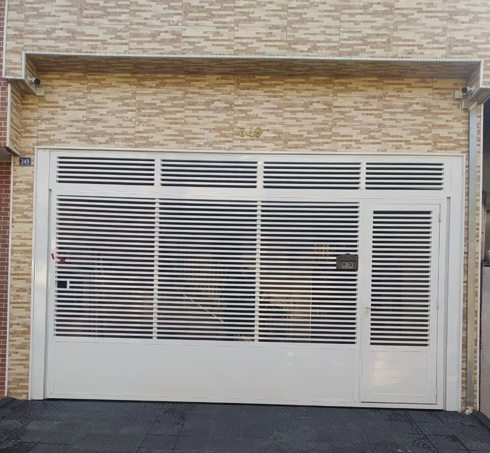 Portão de garagem com veneziana em fachada de tijolinho
